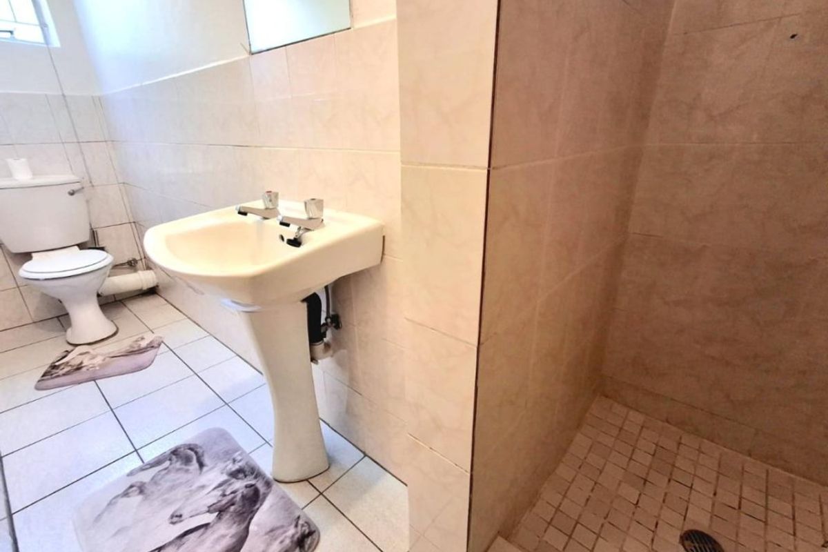 A functional bathroom featuring a pedestal basin, toilet, and a tiled shower enclosure with neutral wall and floor tiling.