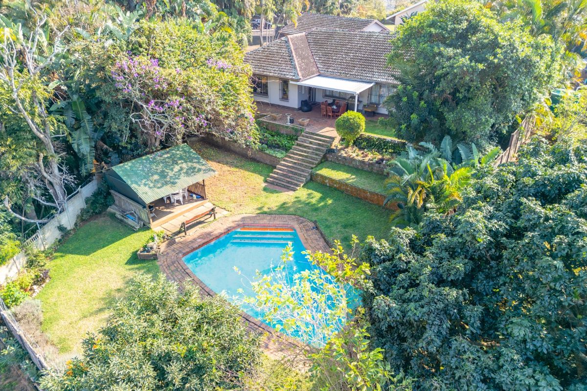 Aerial view of a residential property featuring a swimming pool, landscaped garden, stone retaining walls, and a covered patio area.