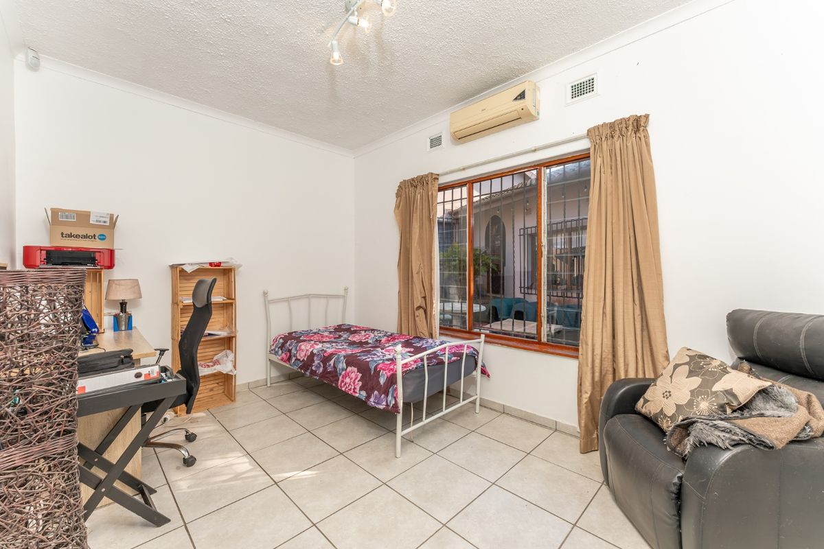 A functional bedroom featuring tiled flooring, a wall-mounted air conditioning unit, and security bars on the window.