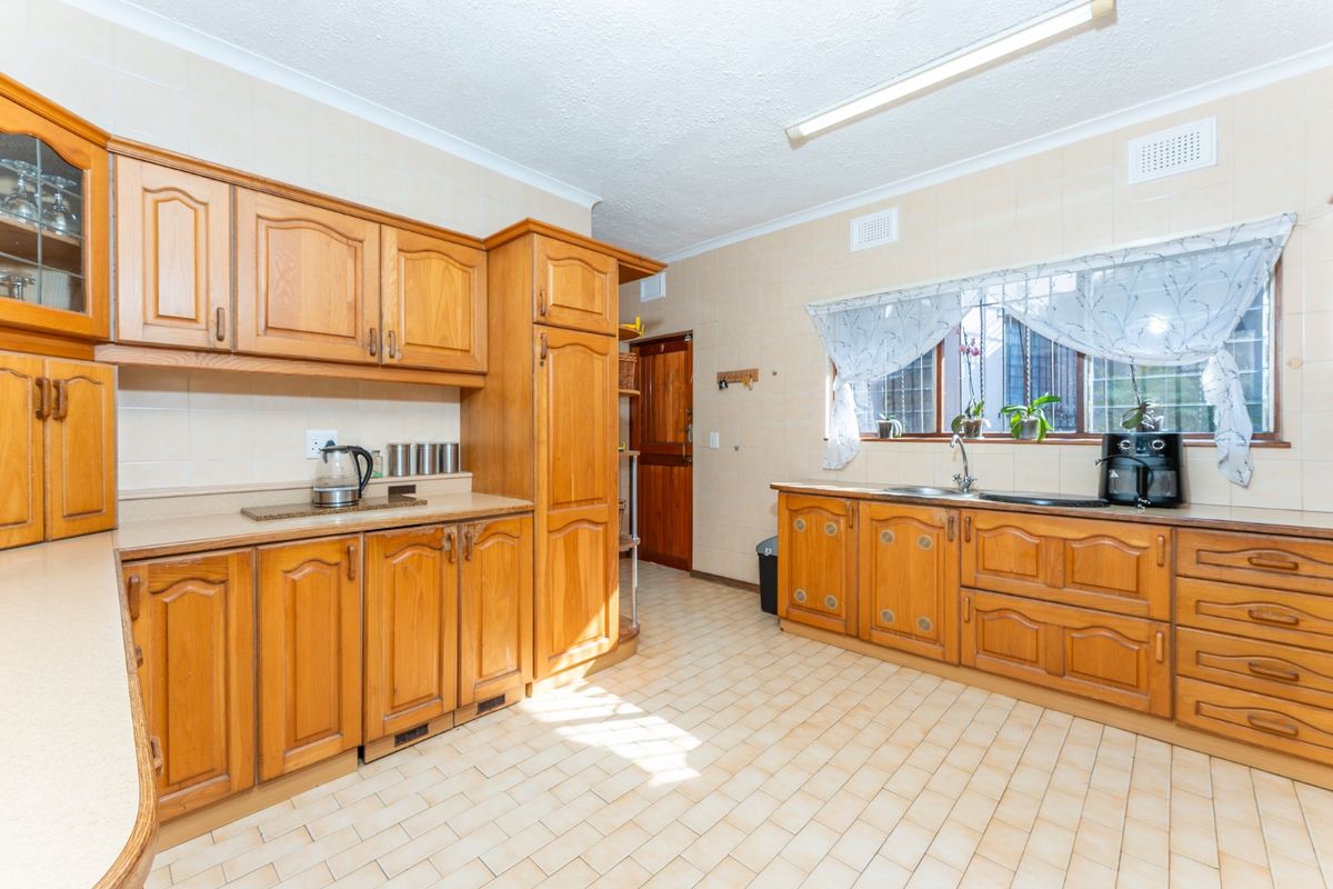 A functional kitchen featuring traditional timber cabinetry, laminate countertops, a double bowl sink, and tiled finishes throughout.