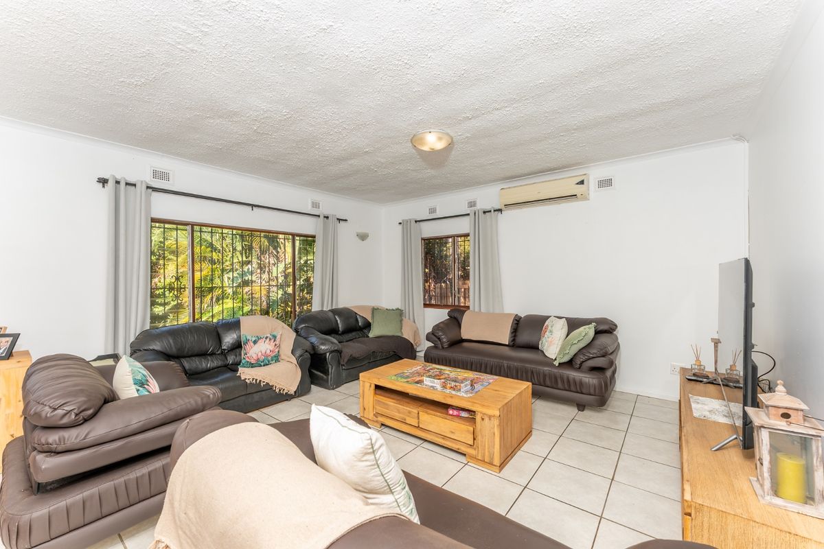 Spacious living room featuring tiled flooring, air conditioning, and large windows with security bars, offering a functional and comfortable family space.