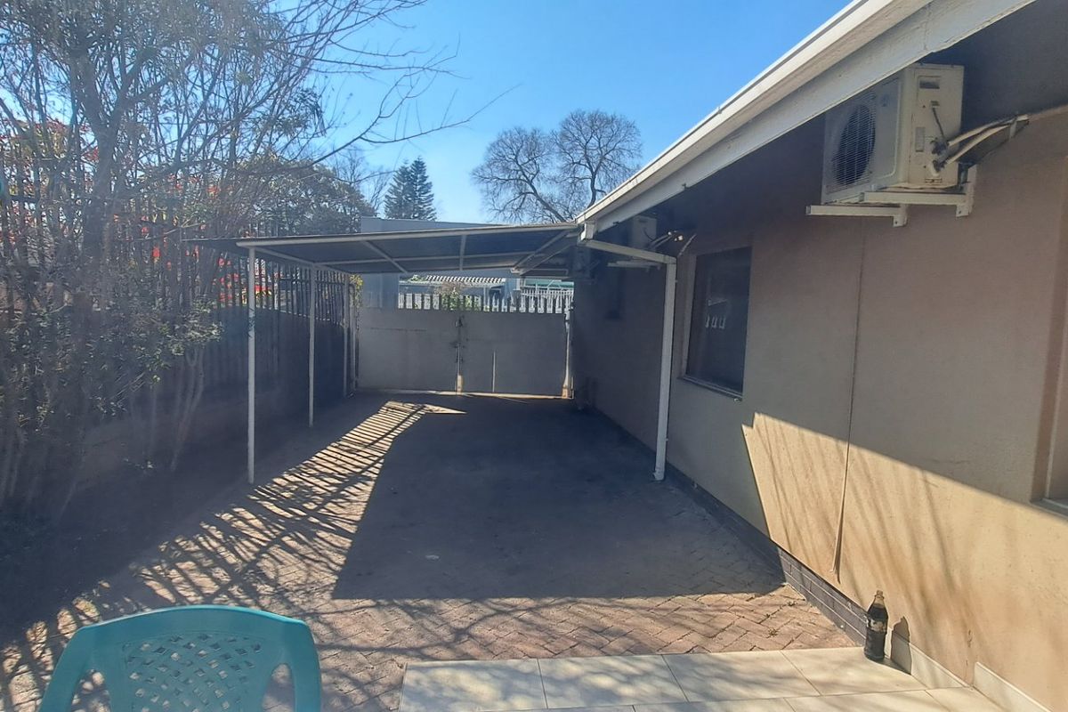Rear exterior area featuring a paved driveway, covered carport, and boundary wall with security gate access.