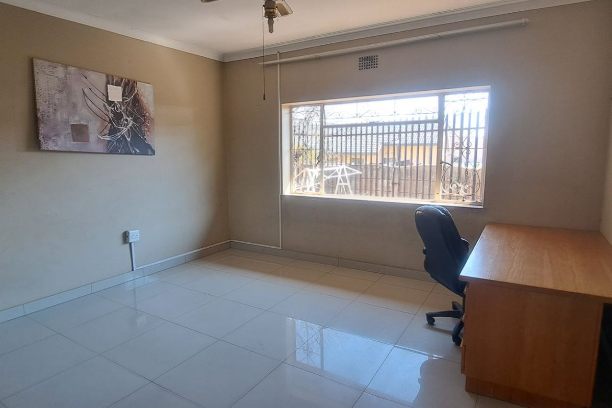 A spacious bedroom featuring tiled flooring, a ceiling fan, and security bars on the window, offering a blank canvas for personalization.