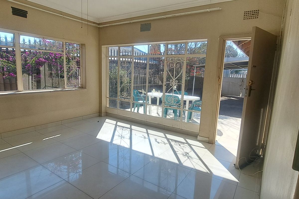 A bright, empty living room featuring large windows with security bars, tiled flooring, and direct access to an outdoor patio area.