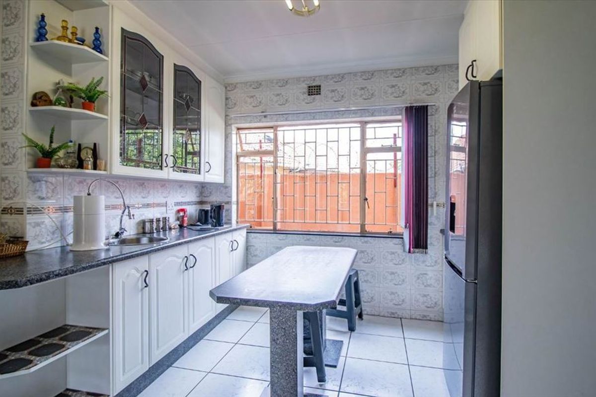 A functional kitchen featuring white cabinetry, tiled splashbacks, a central breakfast bar, and security bars on the window.
