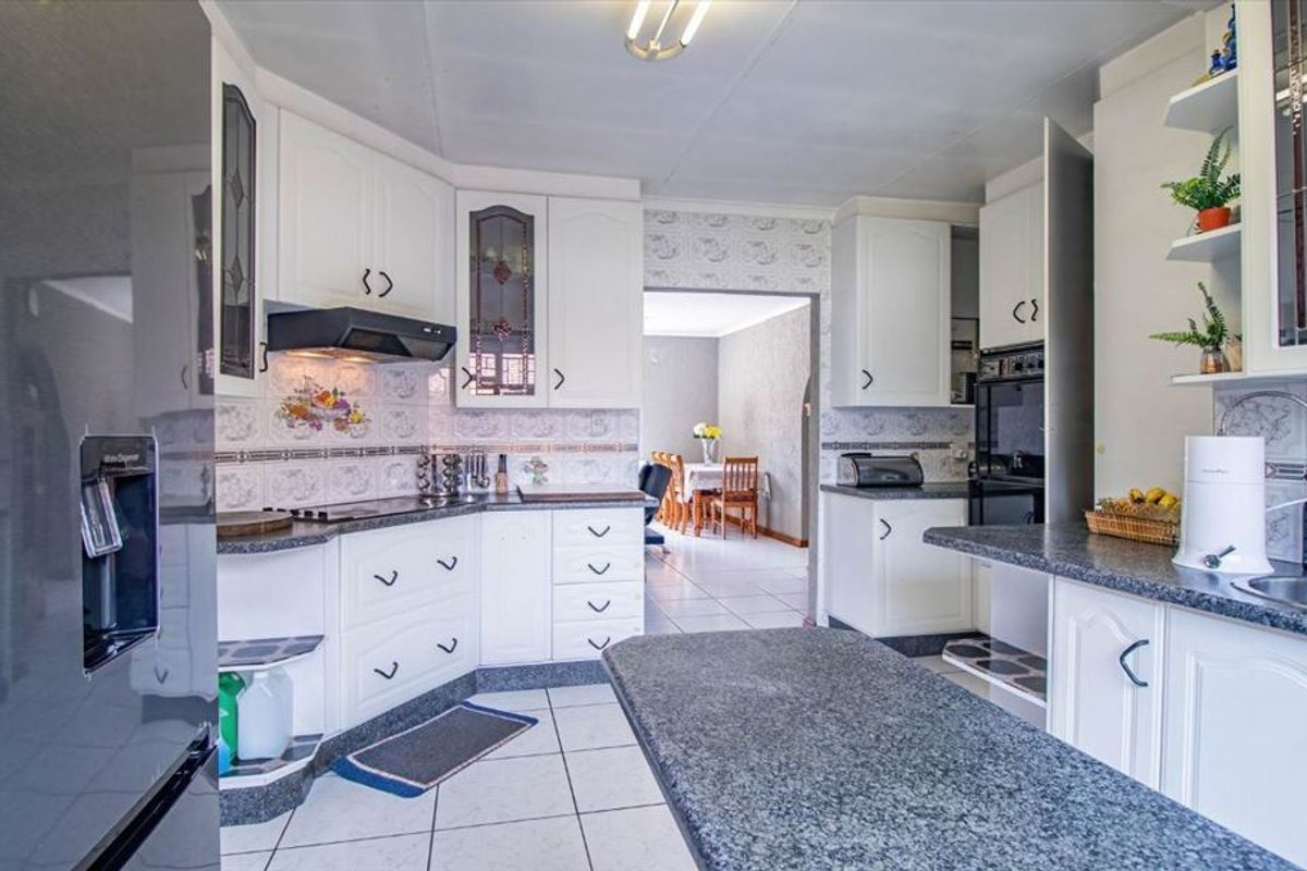 A functional kitchen featuring white cabinetry, granite countertops, tiled backsplash, and built-in appliances, with an open flow to the adjacent dining area.