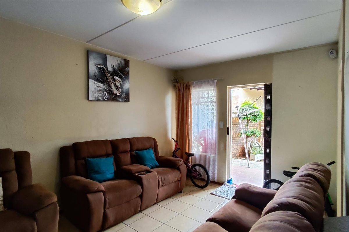 A living room area featuring tiled flooring and direct access to an outdoor patio through a security gate and sliding door.