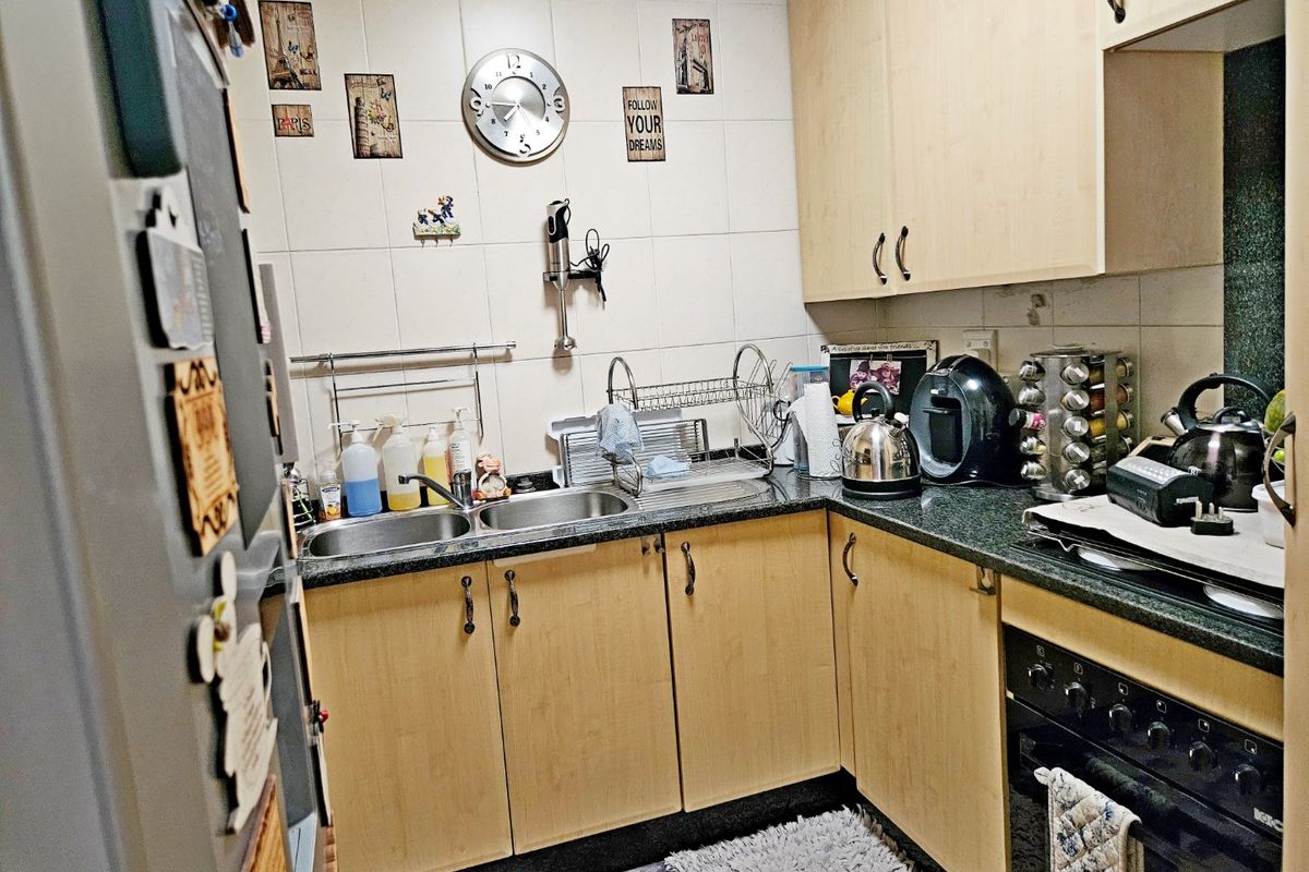 A compact kitchen featuring light wood laminate cabinetry, granite countertops, a double basin sink, and a built-in oven with a tiled backsplash.