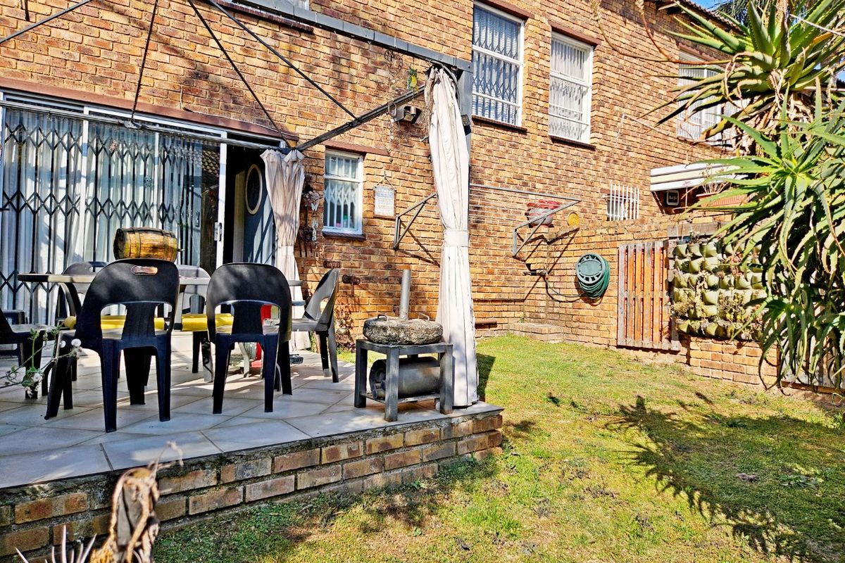 Rear exterior view of a townhouse featuring a brick facade, a paved patio area, and a small garden space.