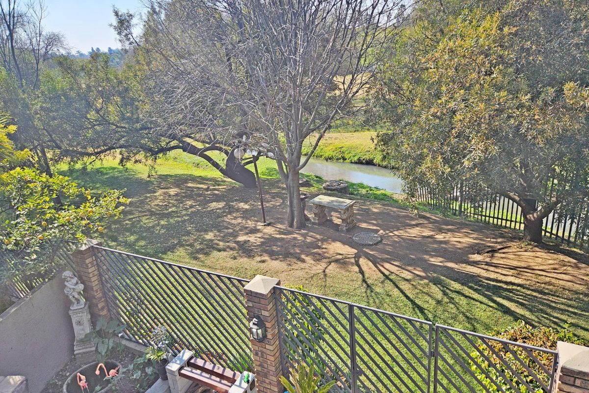 A rear garden view featuring a brick-fenced patio area with a built-in barbecue, overlooking a spacious lawn and a natural stream.