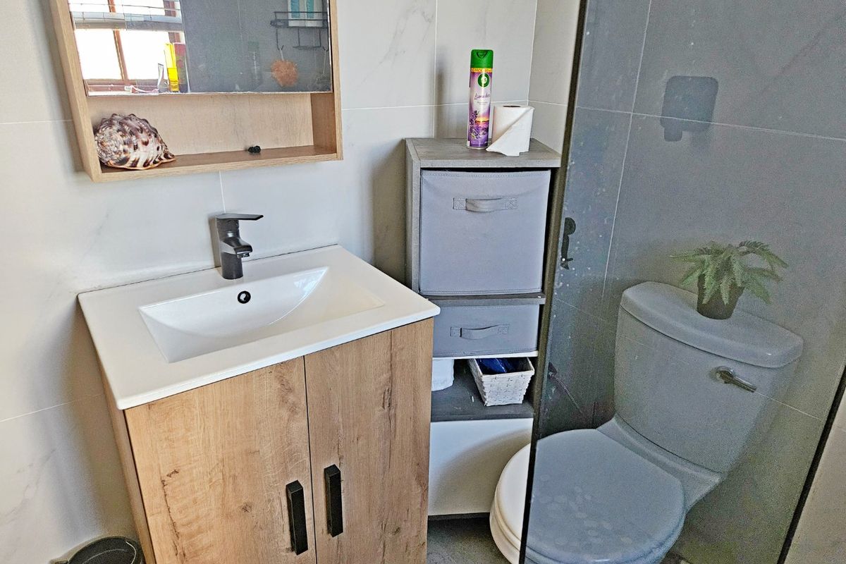 A modern bathroom featuring a wood-finish vanity cabinet, ceramic basin, wall-mounted mirror cabinet, toilet, and a glass-enclosed shower area with tiled finishes.