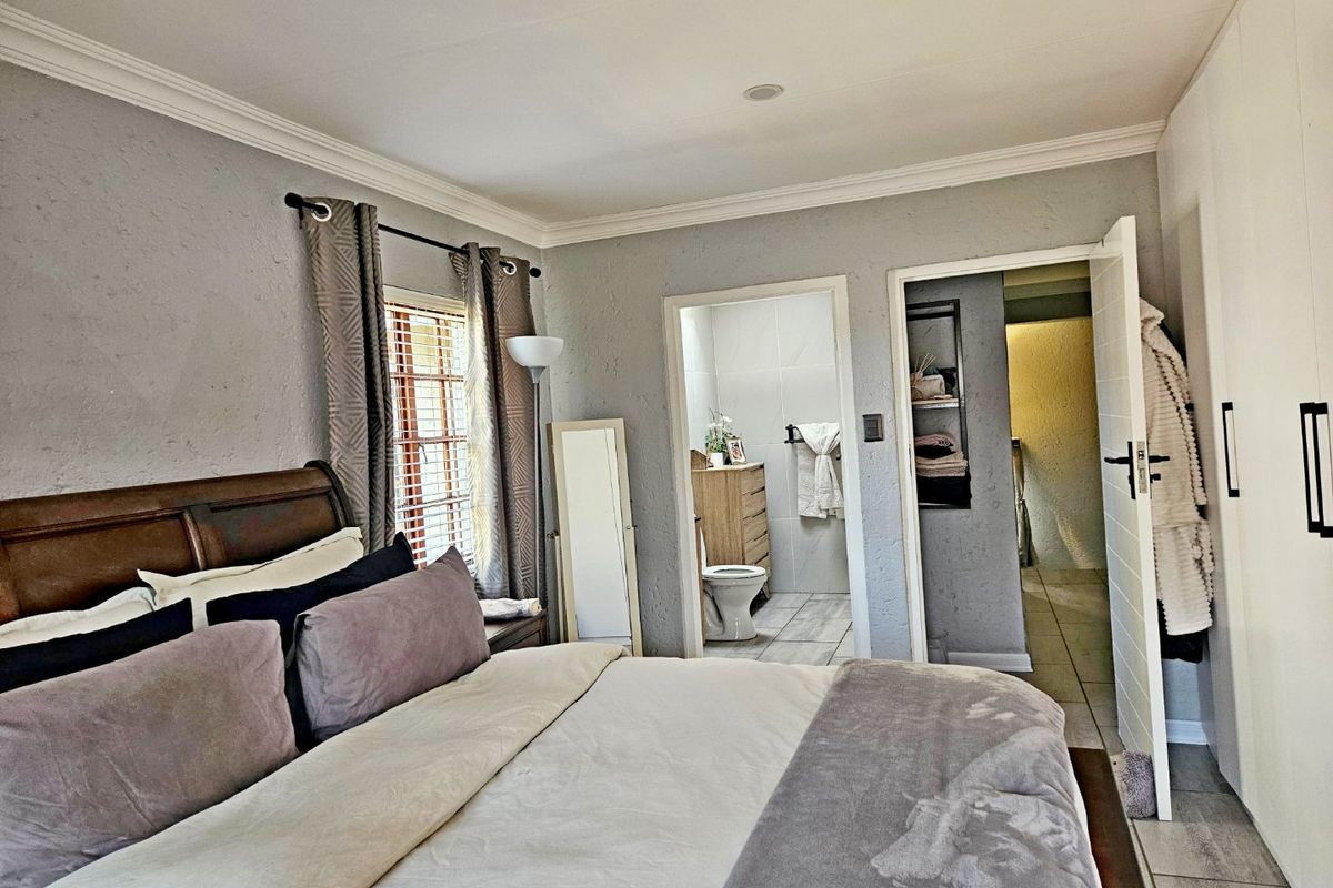 A well-maintained bedroom featuring tiled flooring, cornicing, built-in cupboards, and direct access to an en-suite bathroom.