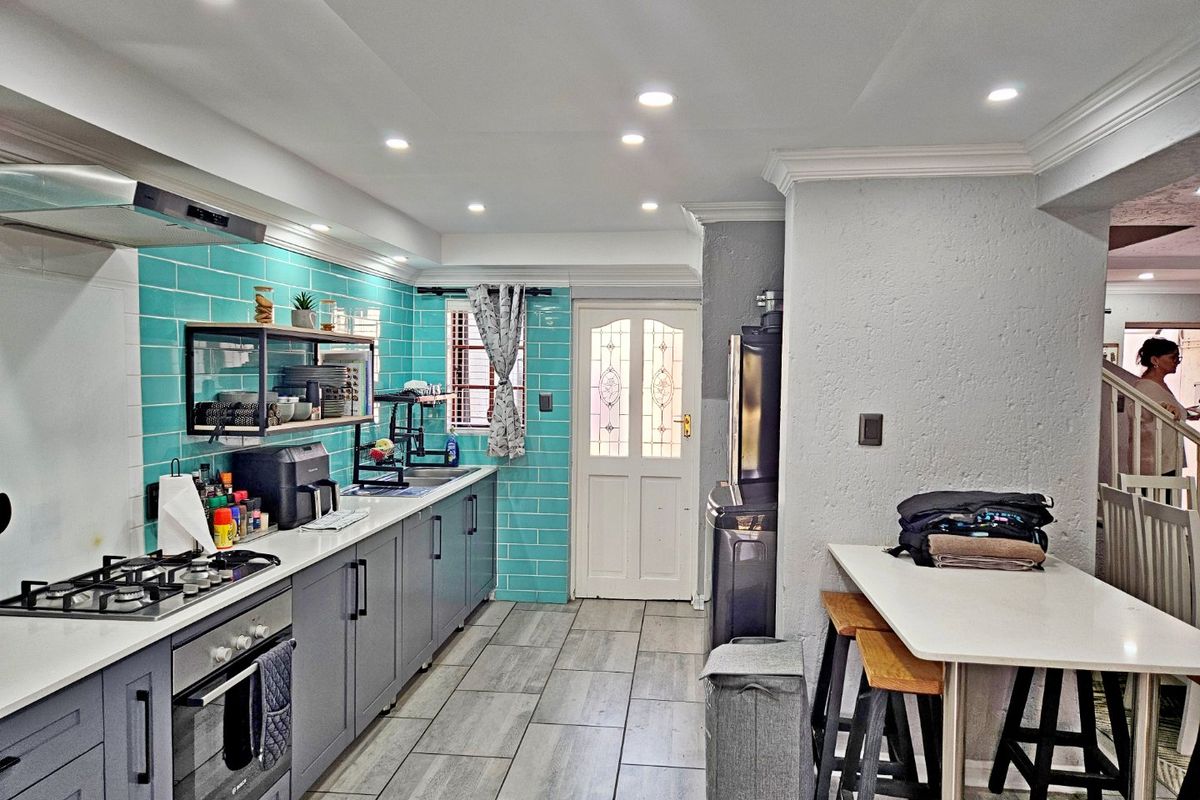 Modern kitchen featuring grey cabinetry, stone countertops, a gas hob, built-in oven, and vibrant turquoise subway tile backsplash with recessed lighting.