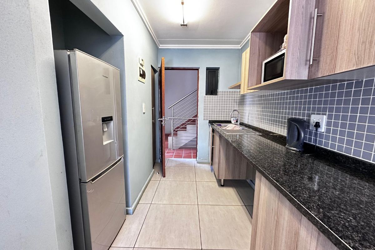 A functional galley-style kitchen featuring granite countertops, tiled backsplash, and modern wood-finish cabinetry with ample storage space.