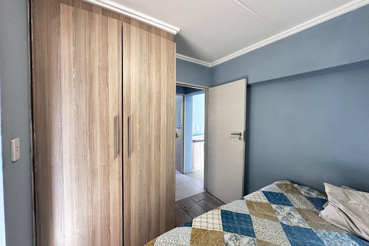 A bedroom featuring a wood-finish built-in wardrobe, blue painted walls, and crown molding, with an open door leading to an adjacent room.