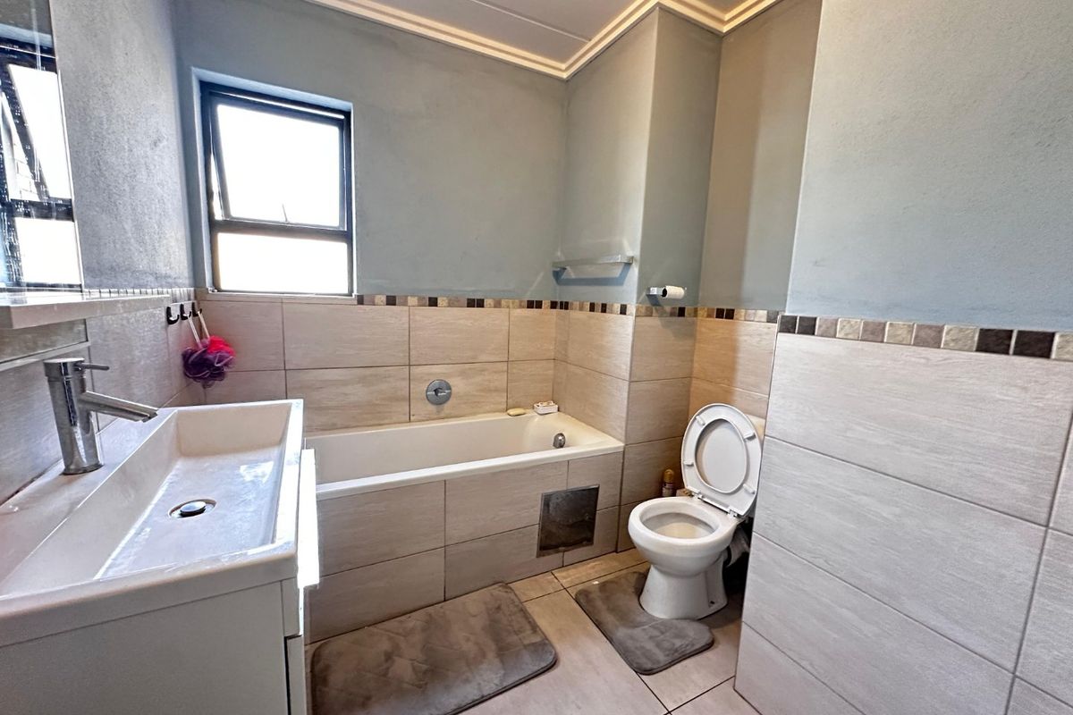 A functional bathroom featuring a bathtub, toilet, and vanity basin with neutral wall and floor tiling.