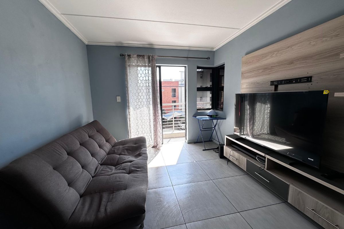 A well-lit living room featuring tiled flooring, a coved ceiling, and a built-in media unit, with direct access to a private balcony.