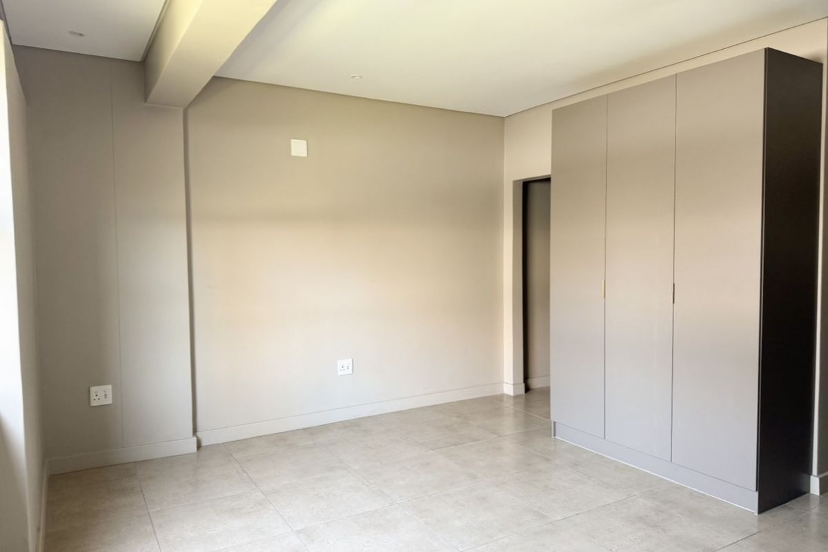 A clean, modern bedroom featuring neutral-toned tiled flooring, recessed ceiling lighting, and ample built-in cupboard storage.