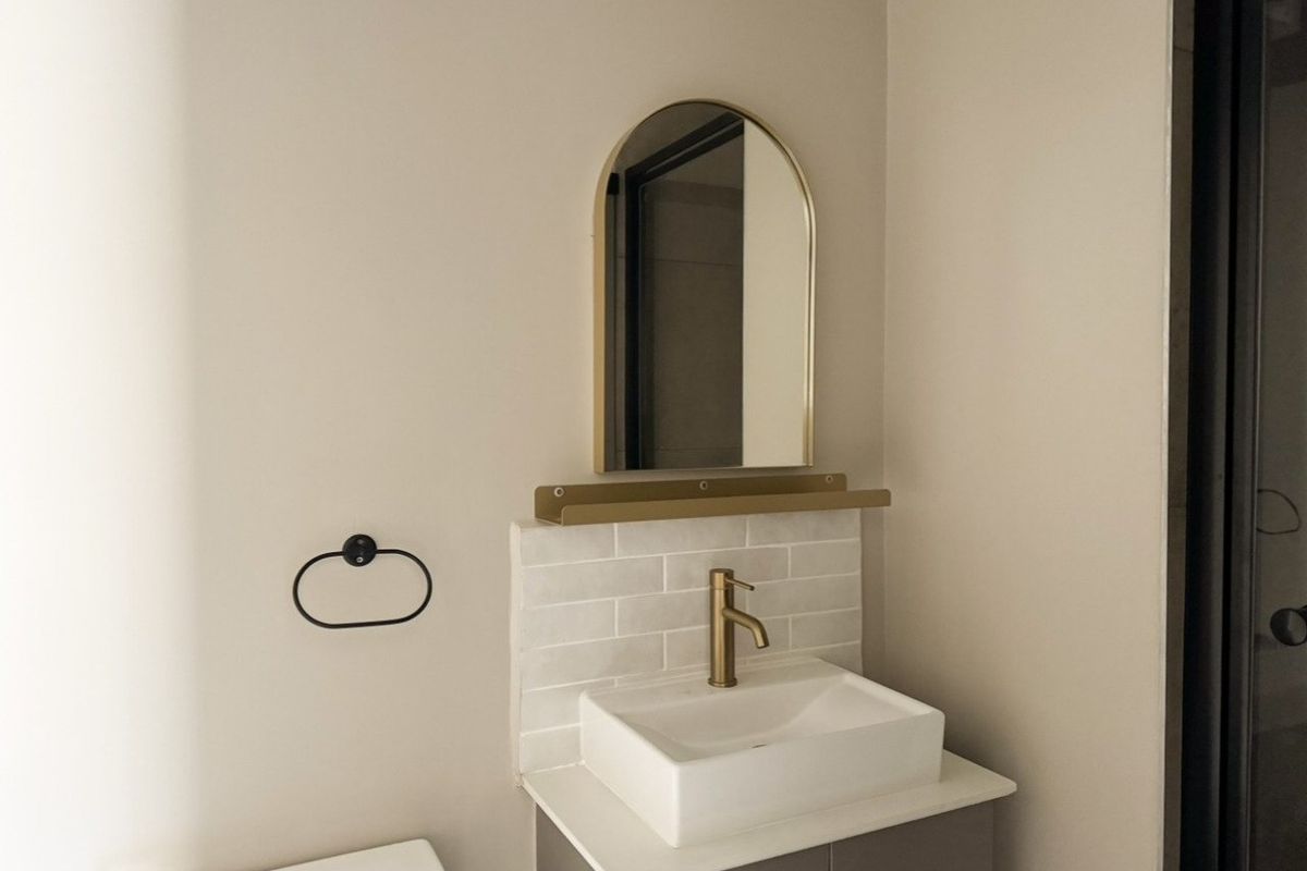 Modern bathroom featuring a sleek vanity with a vessel sink, brass fixtures, subway tile backsplash, and an arched mirror.