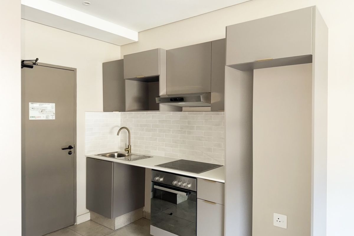 Modern compact kitchen featuring sleek grey cabinetry, subway tile backsplash, integrated electric hob, oven, and extractor fan in a clean, contemporary finish.