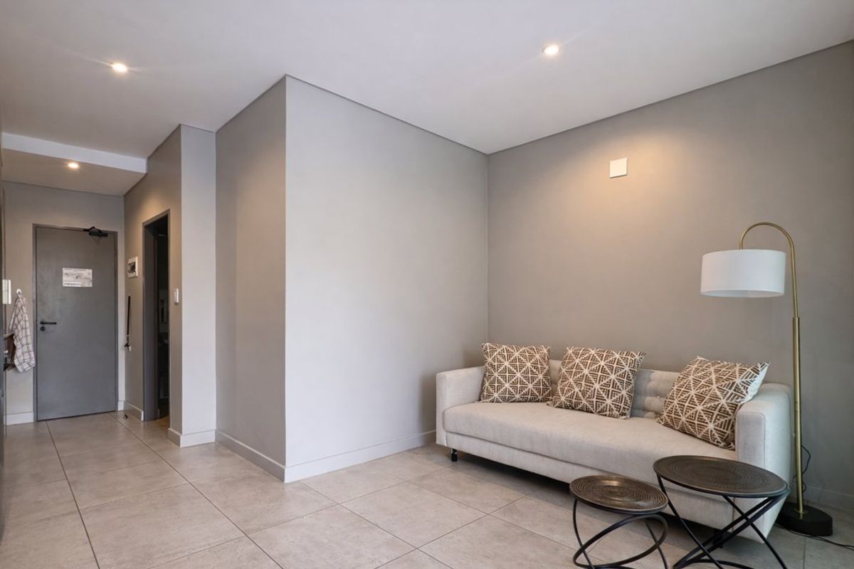 A modern living area featuring neutral grey walls, recessed downlighting, and large format floor tiles, providing a clean and contemporary aesthetic.
