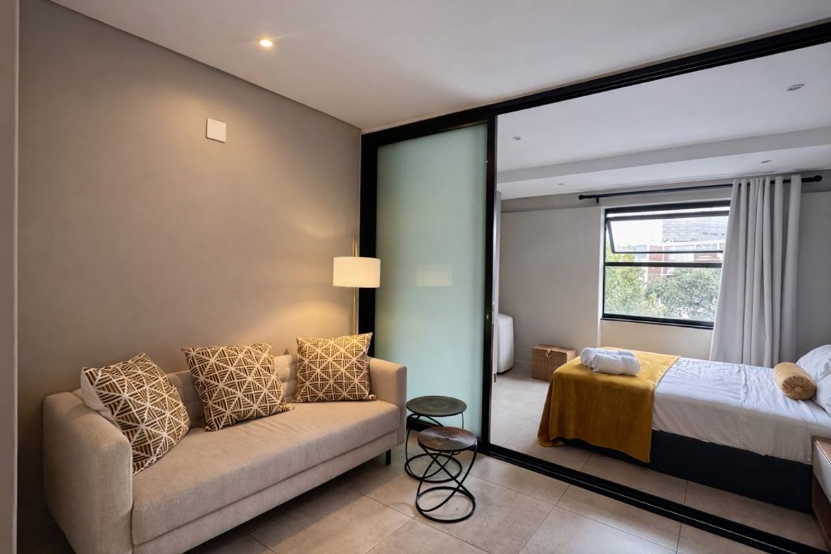 A modern bedroom featuring tiled flooring, recessed lighting, and a sliding glass partition separating the sleeping area from the lounge space.