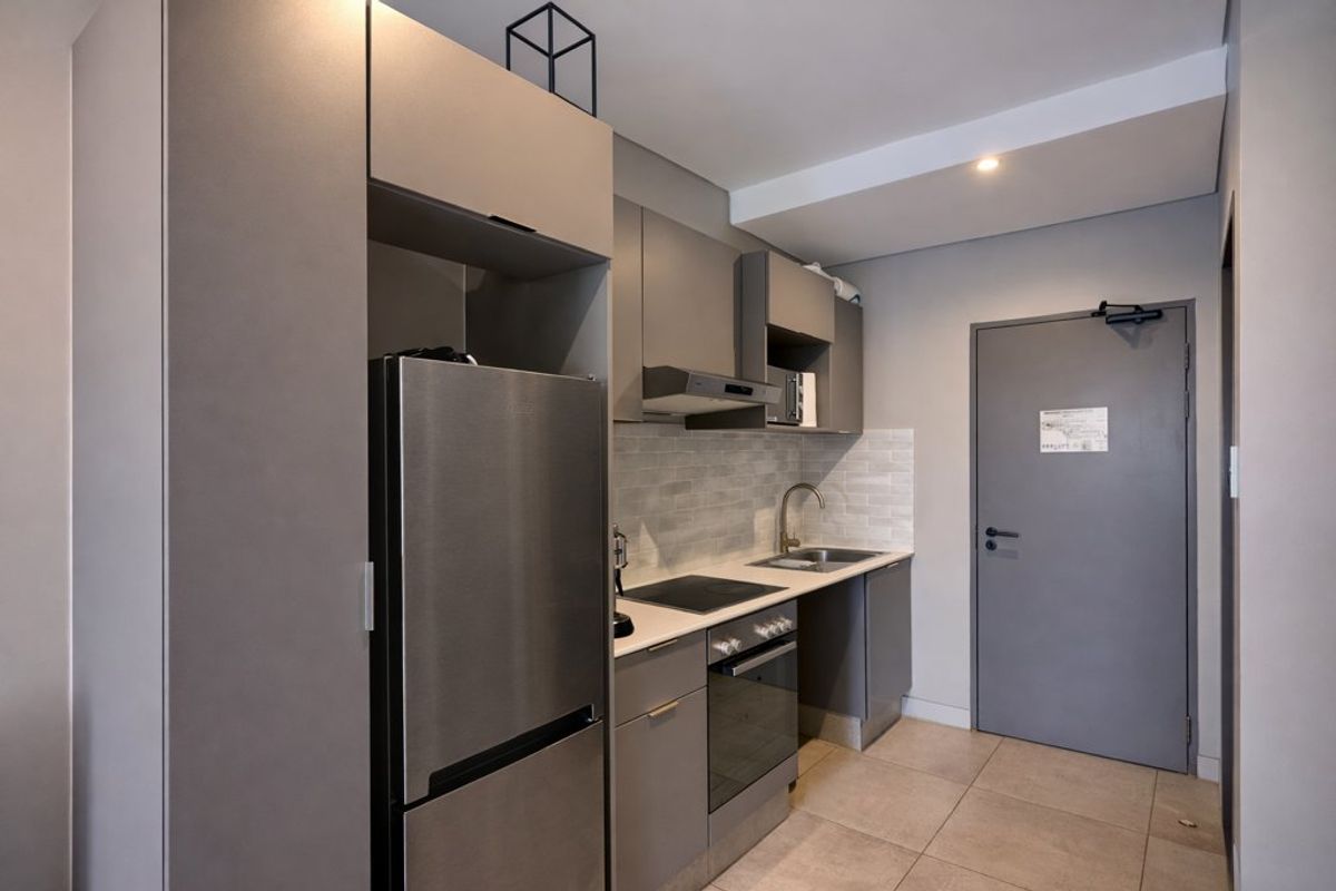 Modern compact kitchen featuring sleek grey cabinetry, integrated appliances, tiled backsplash, and neutral floor tiles.