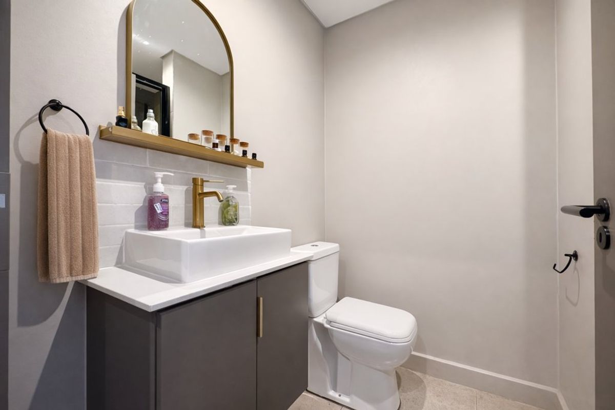 Modern bathroom featuring a sleek vanity with a countertop basin, brass fixtures, subway tile backsplash, and an arched mirror.