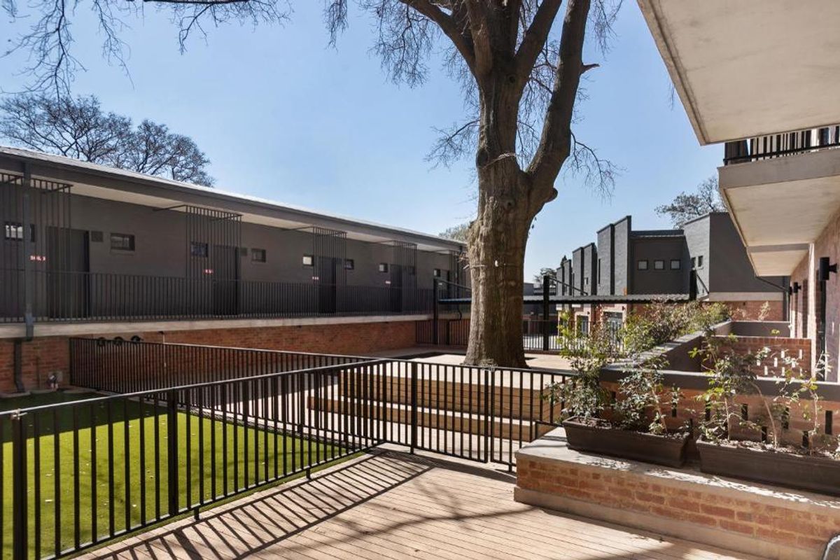 A well-maintained communal courtyard area featuring timber decking, artificial lawn, and mature landscaping within a modern apartment complex.