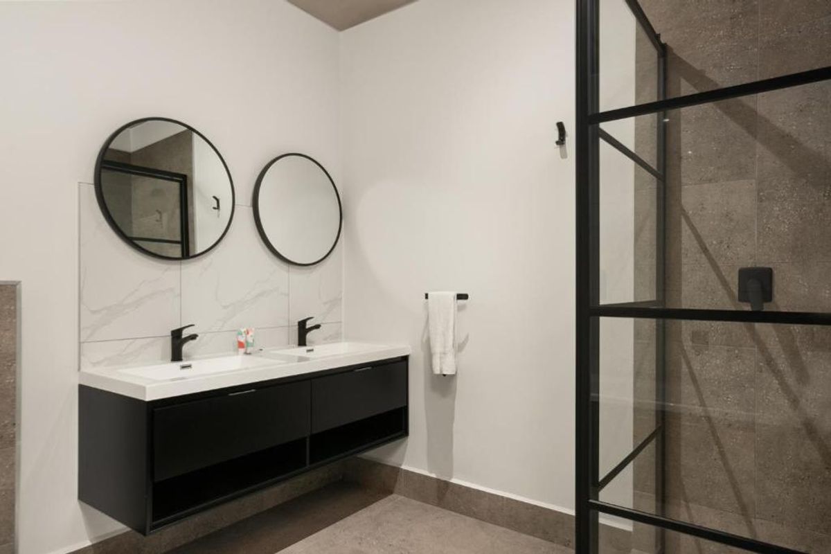 Modern bathroom featuring a sleek double vanity with wall-mounted cabinetry, marble-look splashback, and a spacious walk-in shower with a black-framed glass screen.