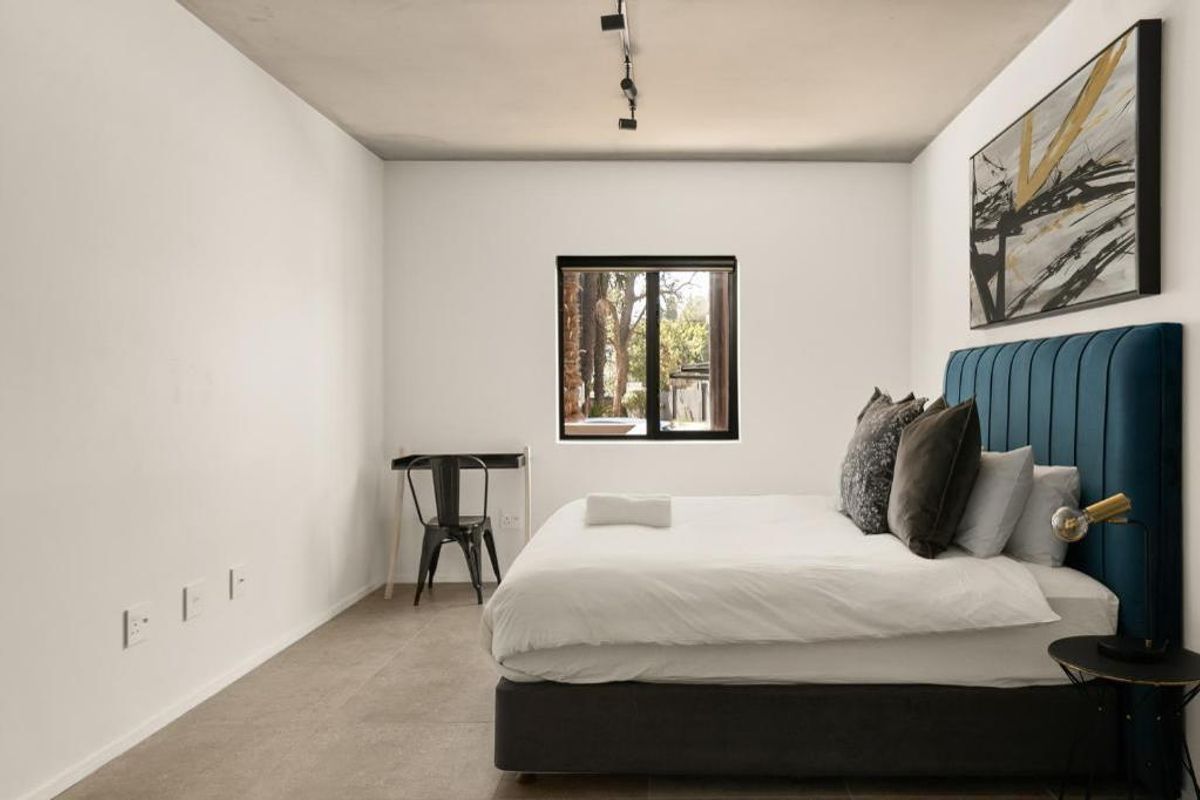 A modern bedroom featuring neutral tiled flooring, a black-framed window, and minimalist track lighting, creating a clean and contemporary living space.