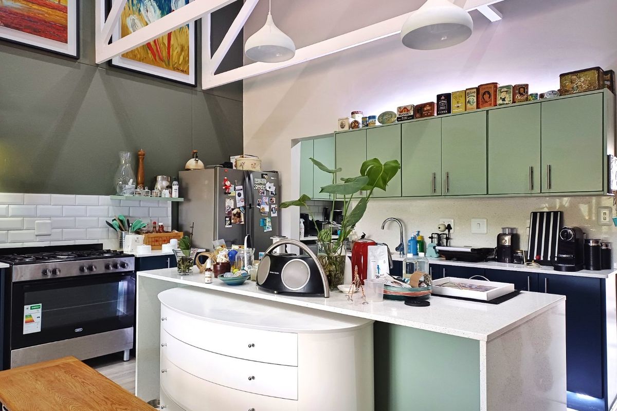 Modern kitchen featuring sage green cabinetry, quartz countertops, a central island, subway tile backsplash, and high ceilings with exposed white roof trusses.