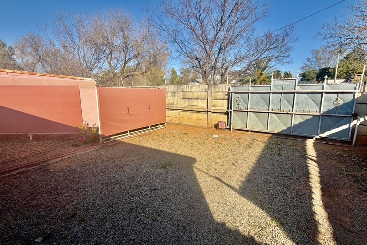 A spacious rear yard featuring a gravel surface, paved patio section, and secure perimeter walling with a large metal sliding gate.