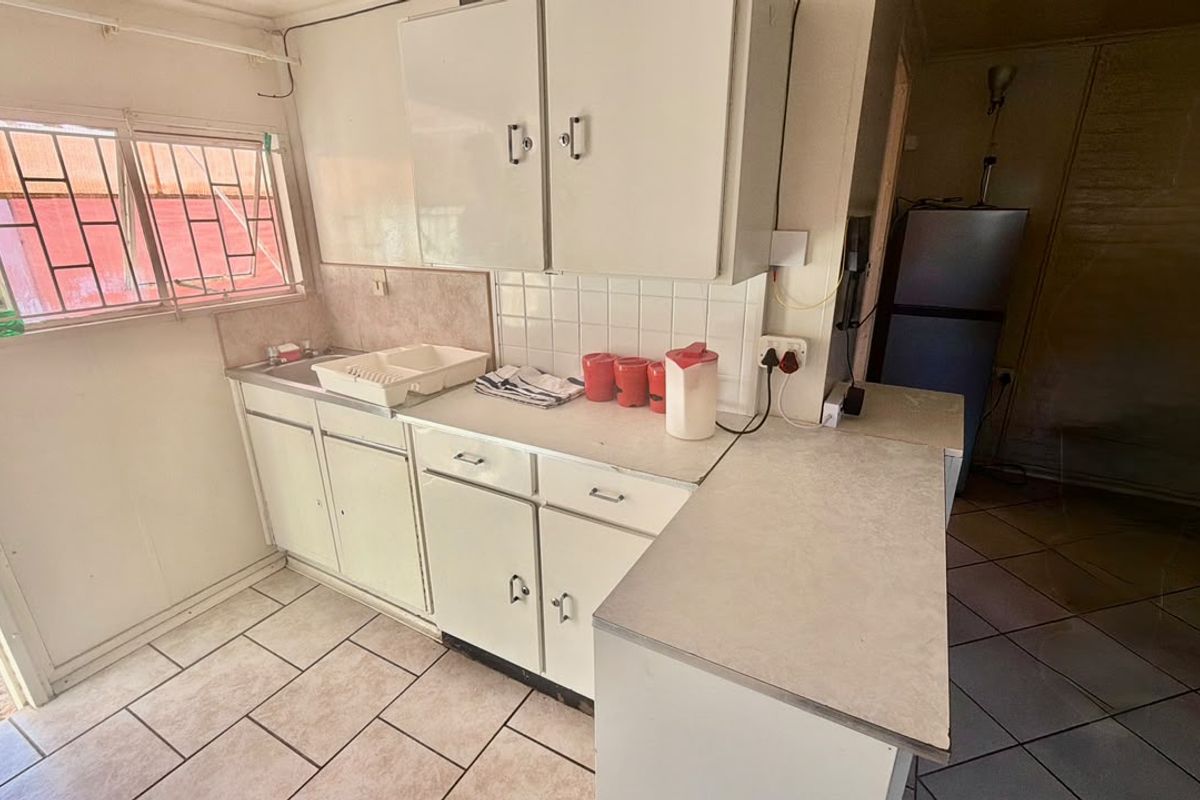 A functional kitchen featuring built-in cabinetry, laminate countertops, a stainless steel sink, and tiled flooring, offering potential for modernization.