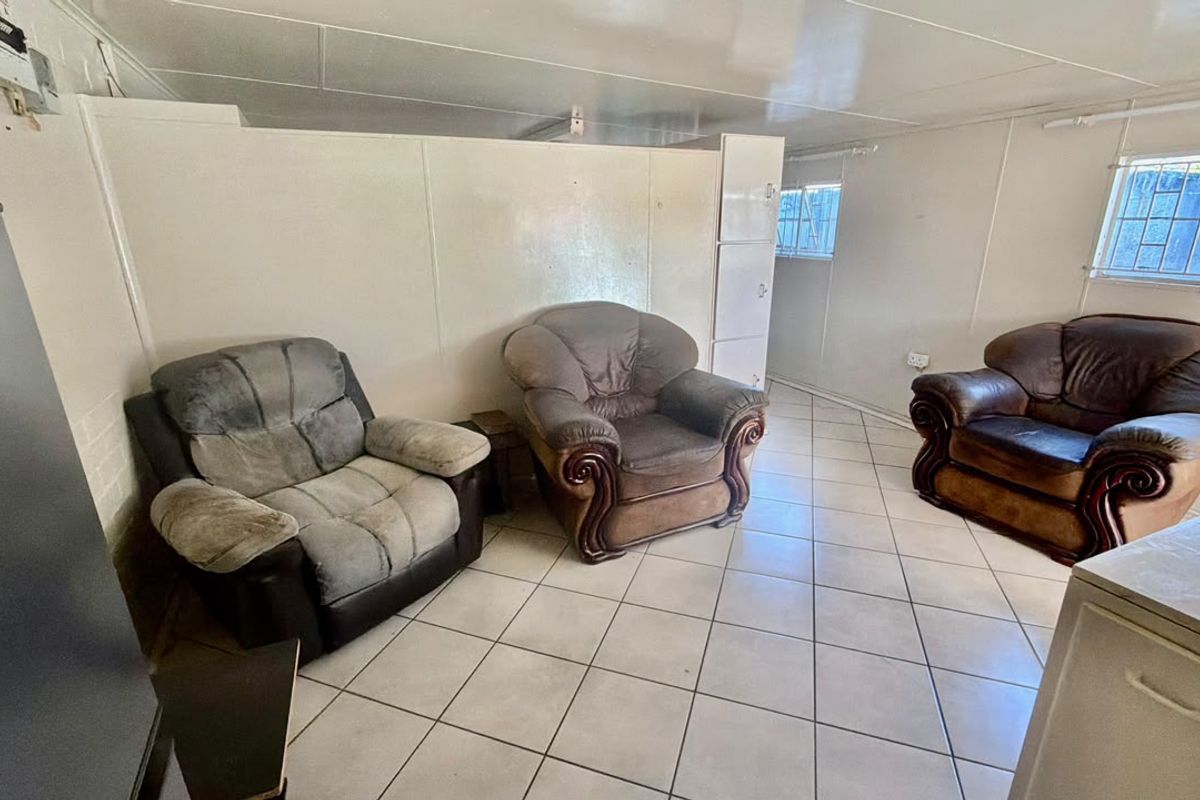 A living area featuring tiled flooring, security bars on windows, and a built-in storage cupboard, offering a functional space with potential for modernization.