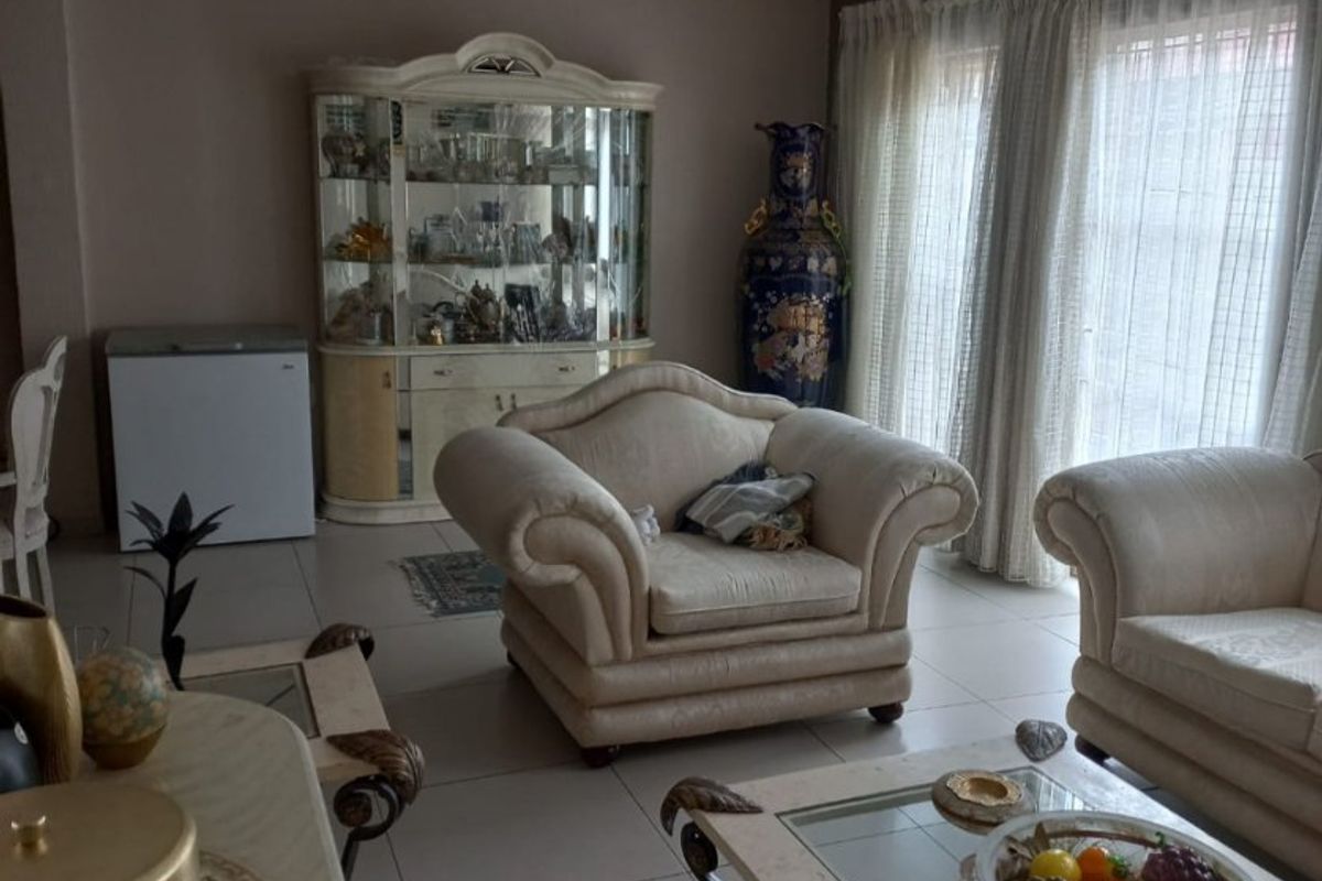 A spacious living room featuring neutral tiled flooring and large windows with curtain tracks, offering a bright and functional living space.