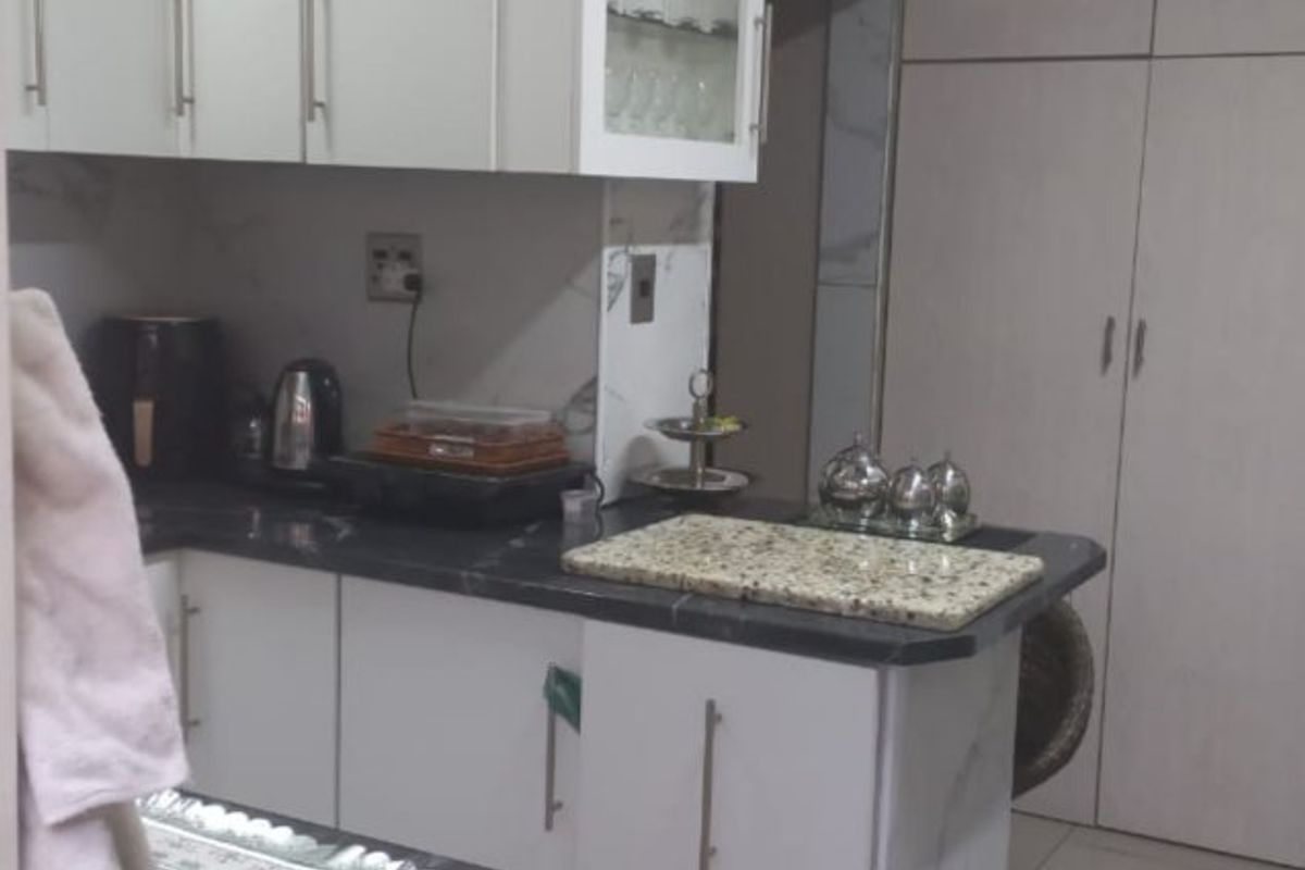 A functional kitchen featuring white cabinetry, dark stone countertops, glass-fronted display units, and ample built-in pantry storage with tiled flooring.
