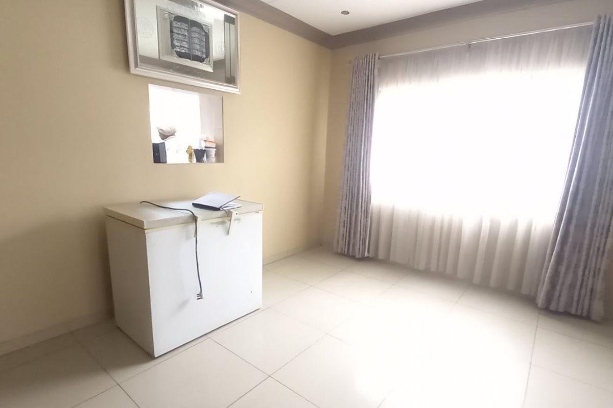 A bright, neutral-toned living area featuring tiled flooring, recessed ceiling lighting, and a built-in wall niche, offering a clean and versatile space.