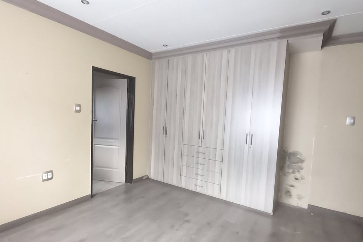 Empty bedroom featuring light-toned built-in cupboards, laminate flooring, and recessed lighting. The room requires minor wall repairs and maintenance.