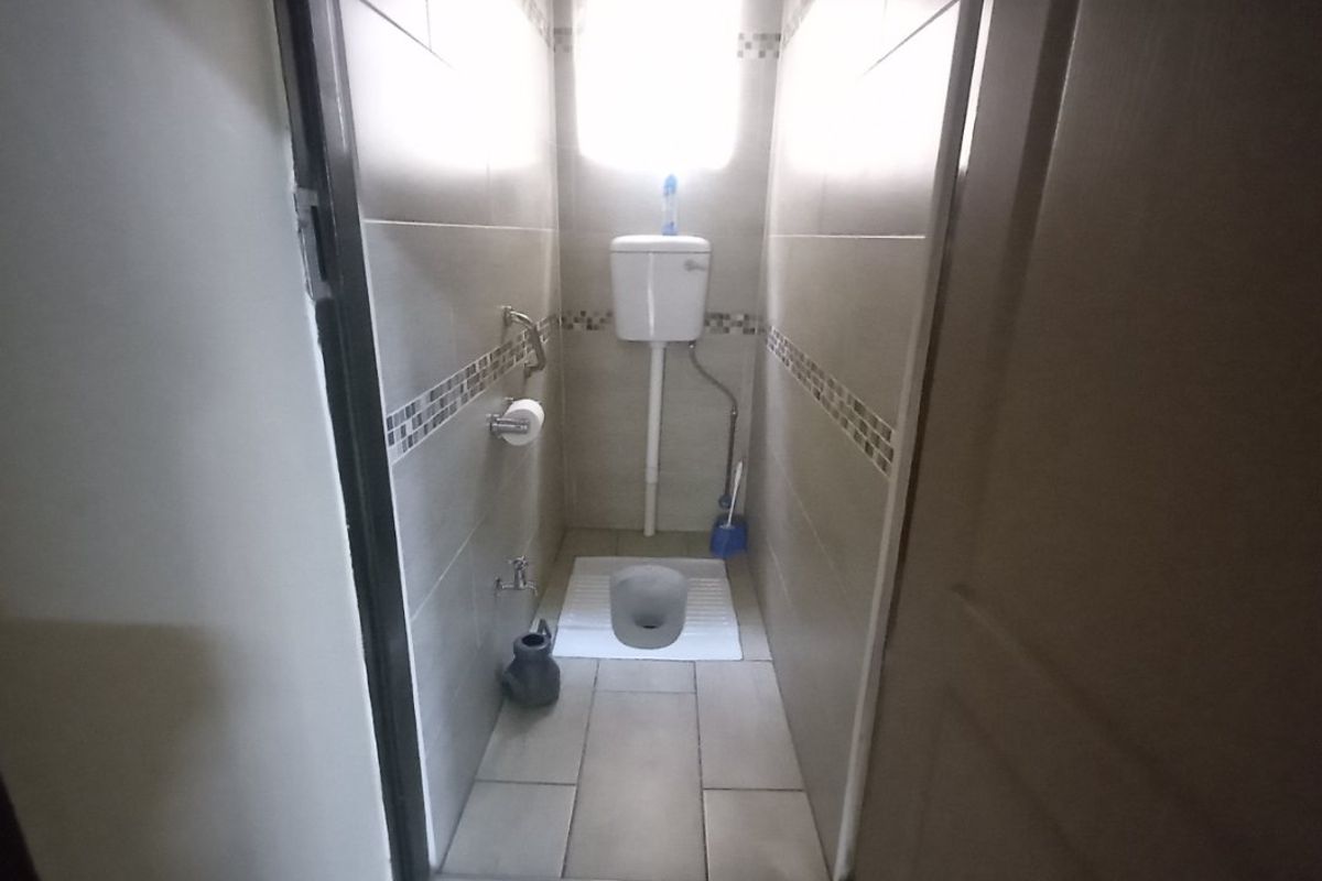 A compact bathroom featuring a squat toilet, neutral ceramic wall and floor tiling, and a high-level cistern.
