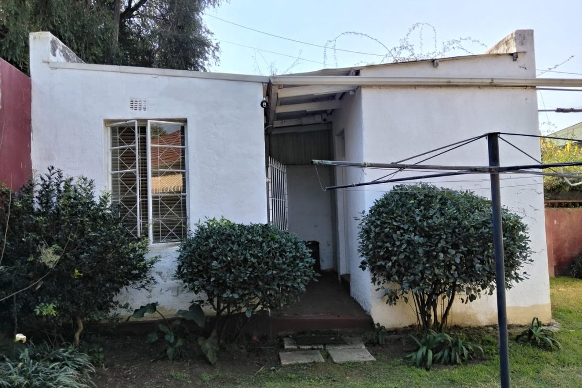 Rear exterior view of the property featuring a white rendered facade with security bars on the window and a small concrete entrance area.