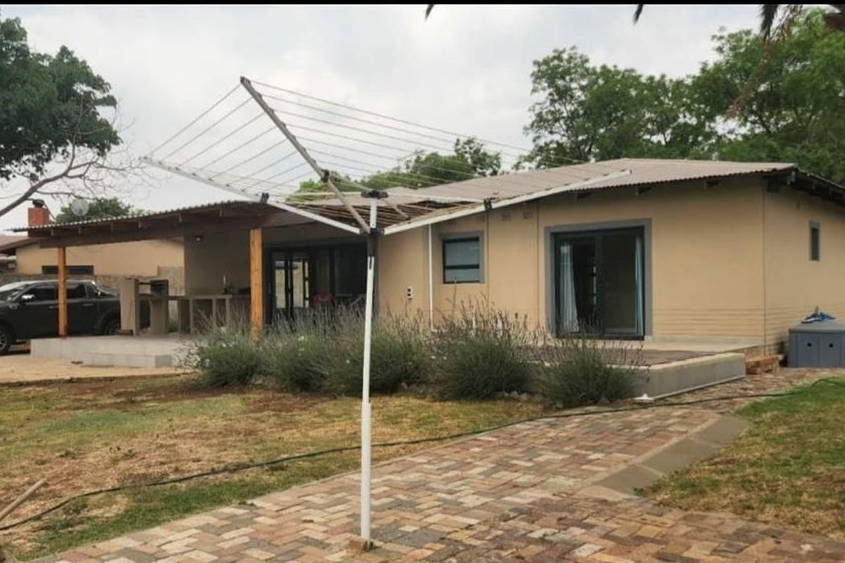 Rear view of the house featuring a covered patio with a built-in braai, sliding glass doors, and a brick paved walkway leading to the entrance.