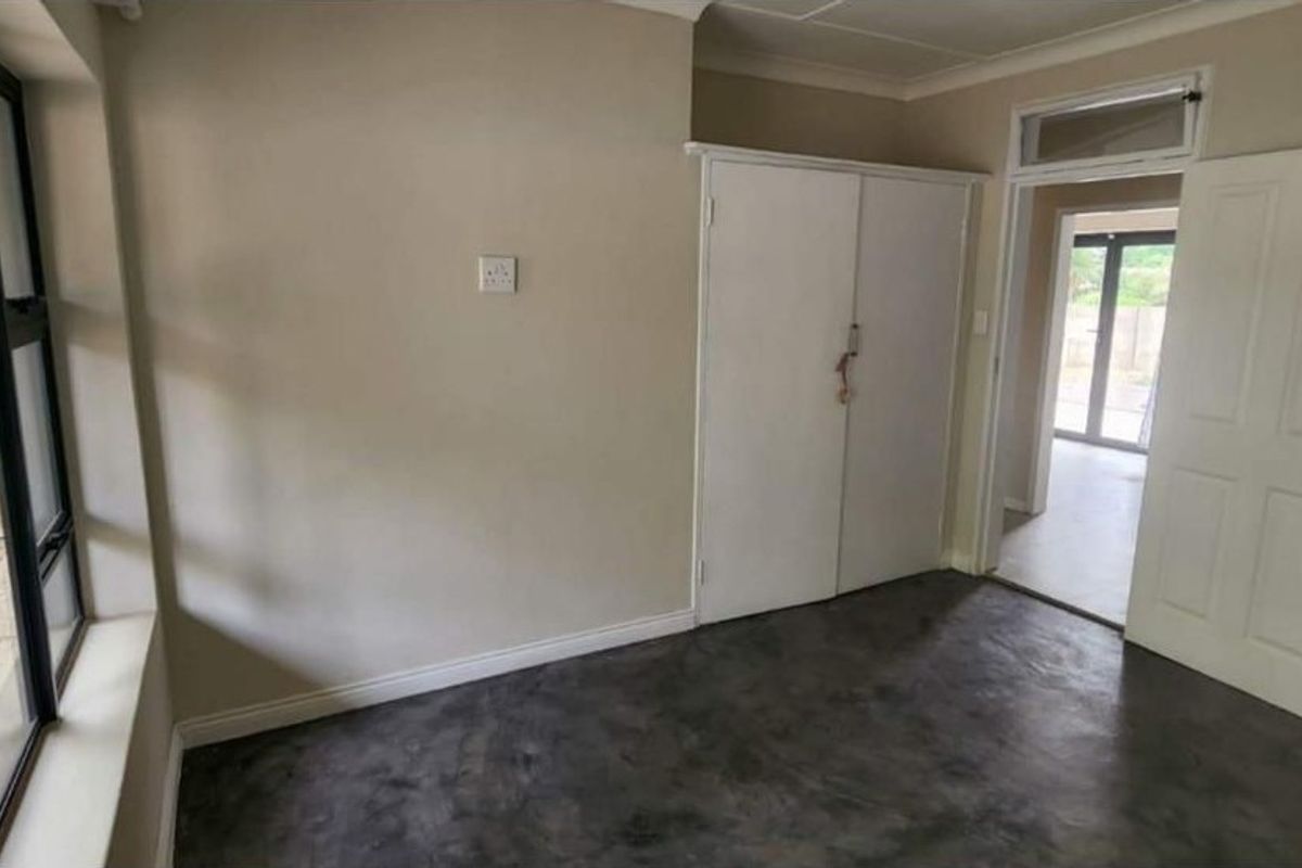 An empty bedroom featuring a built-in cupboard, screeded concrete flooring, and large windows providing natural light.