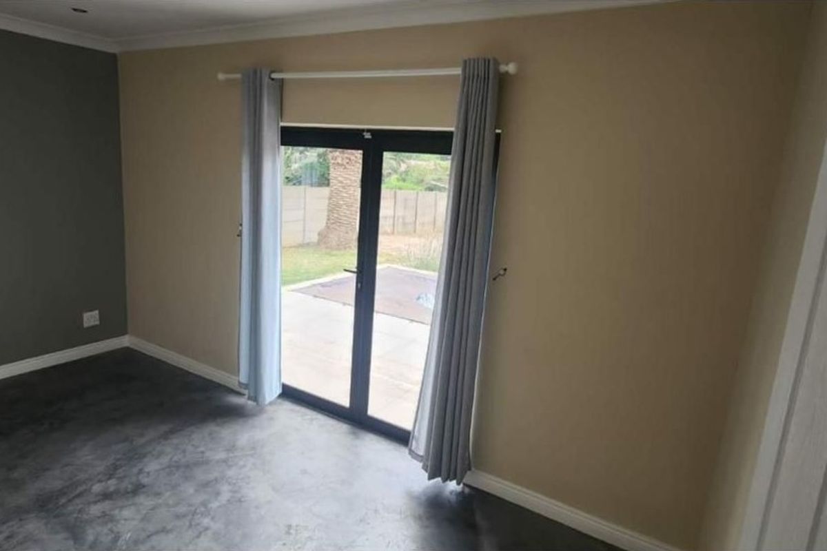 An empty living room featuring polished concrete floors and double glass doors providing direct access to the rear garden area.
