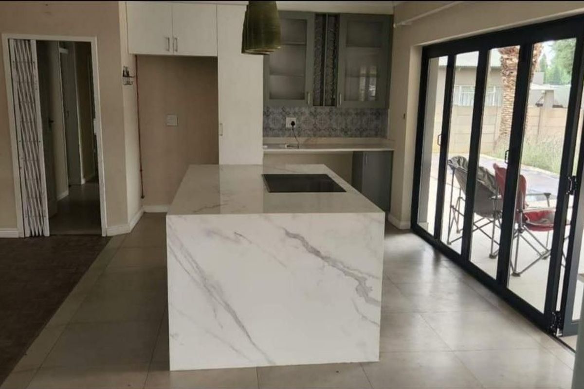 Modern kitchen featuring a large stone-topped island with integrated hob, sleek cabinetry, and expansive bi-fold doors opening to the outdoor area.