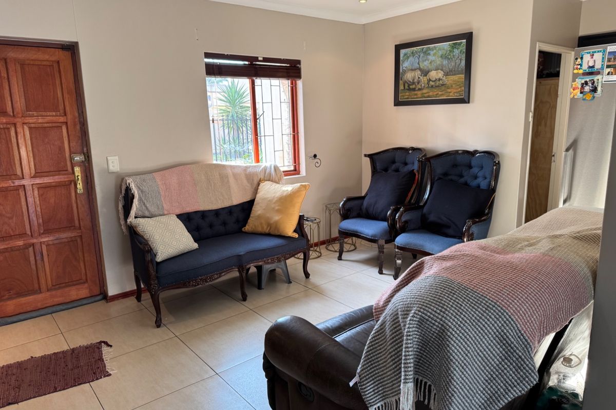 A living room featuring tiled flooring, a timber entrance door, and a window with security bars, providing a functional and well-lit living space.