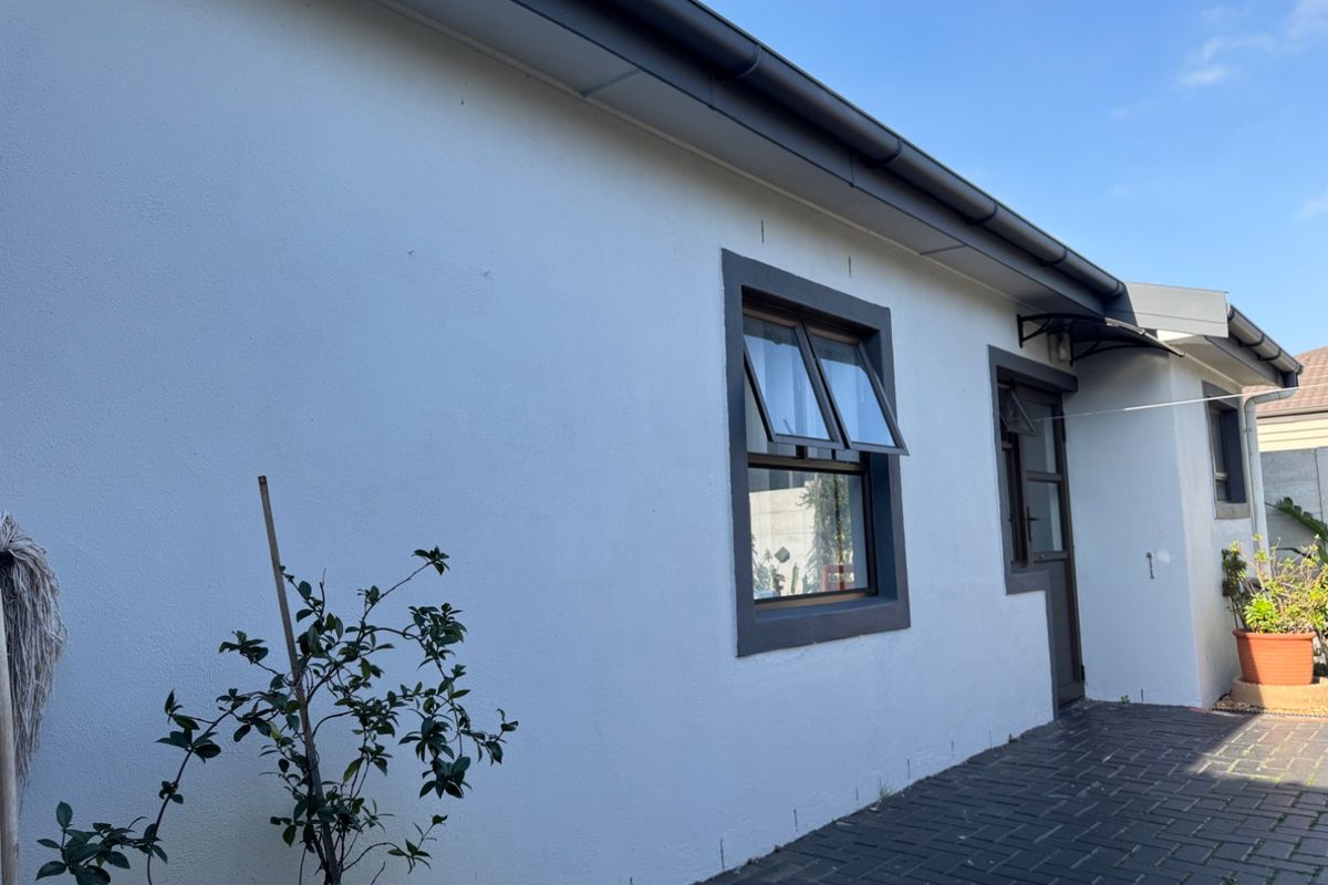 A view of the rear exterior wall featuring a paved patio area, dark-framed casement windows, and a small protective awning over the doorway.