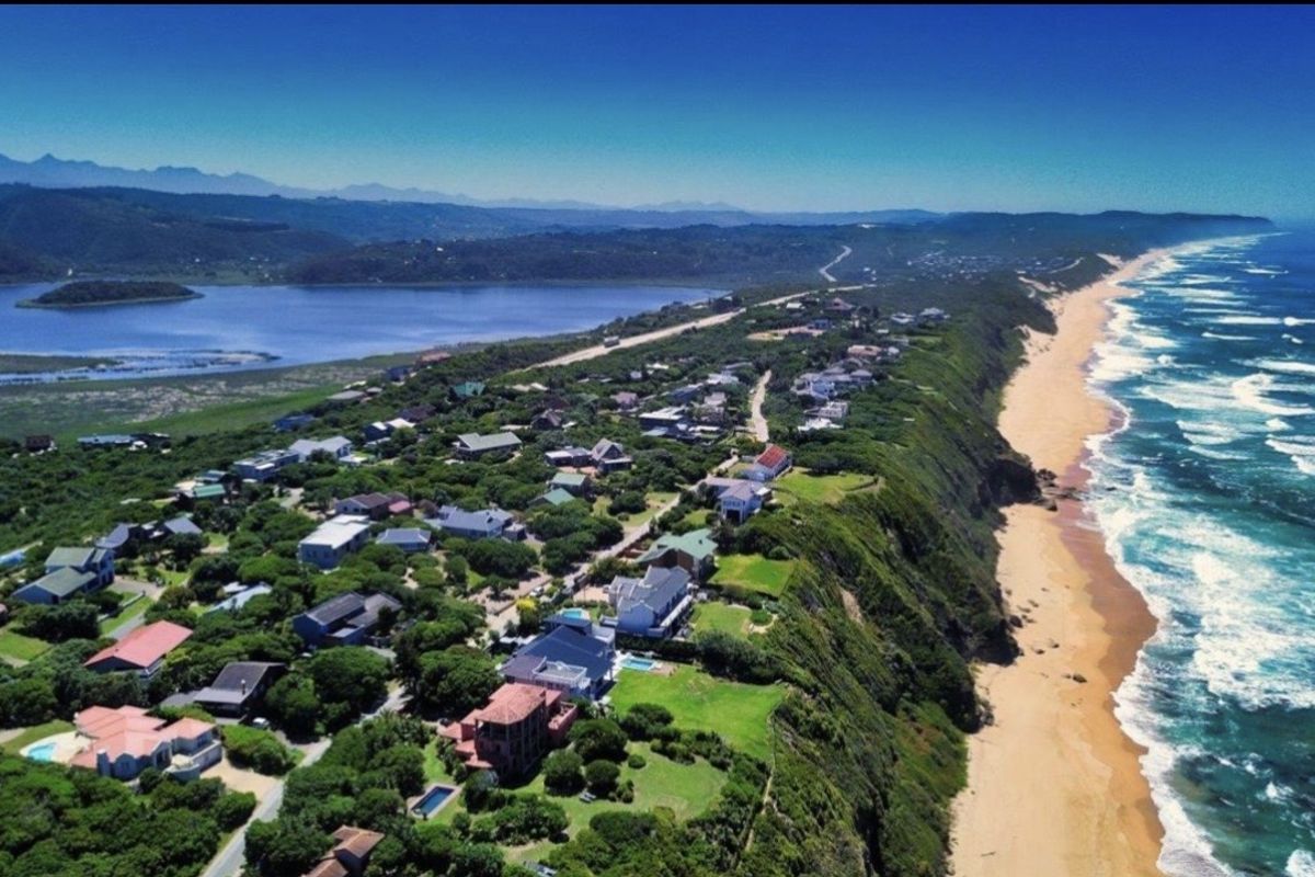 An expansive aerial view of a coastal residential estate situated along a cliffside, overlooking the ocean and nearby lagoon.