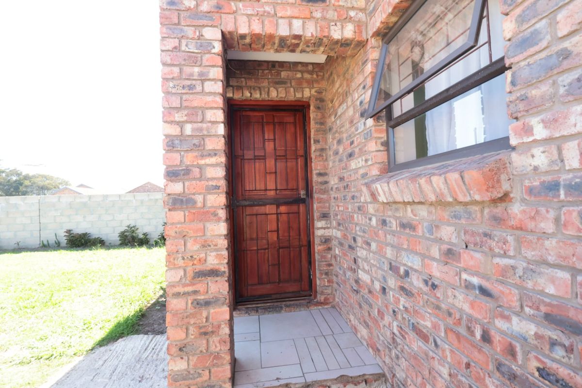 Rear exterior view featuring a face brick facade, a timber security door, and a small tiled porch area overlooking the garden.