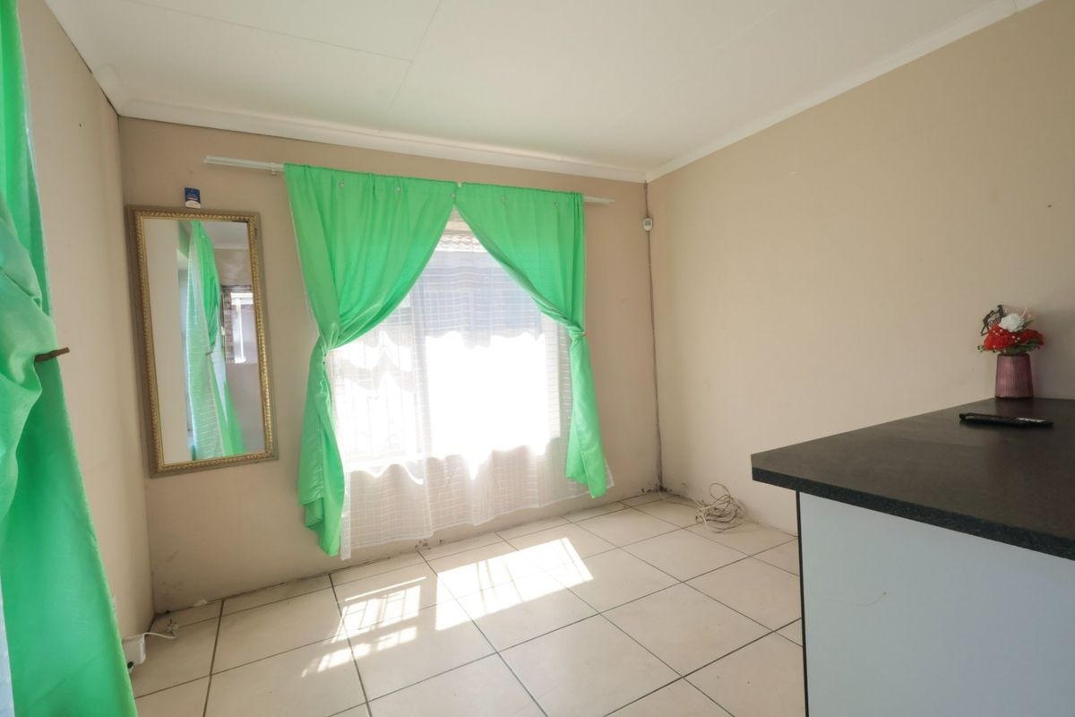 A sparsely furnished living area featuring tiled flooring and a window with curtain rods, showing signs of wear on the lower wall sections.